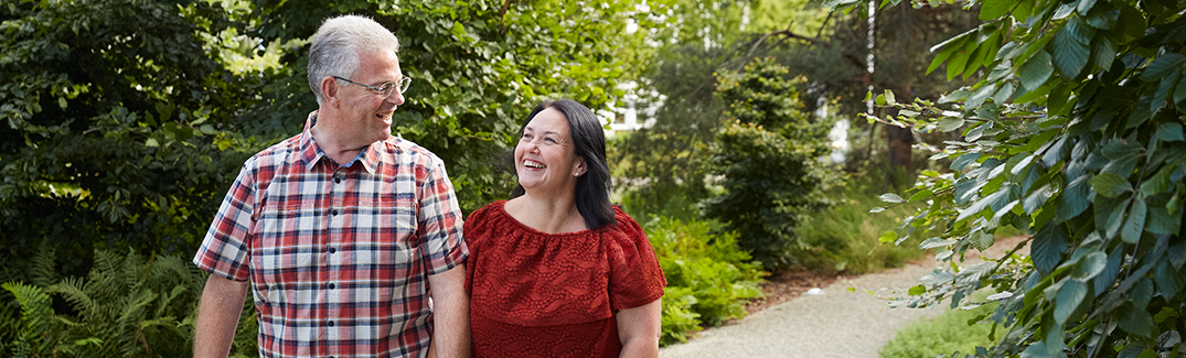 Happy couple walking down a small path through a park, holding hands.