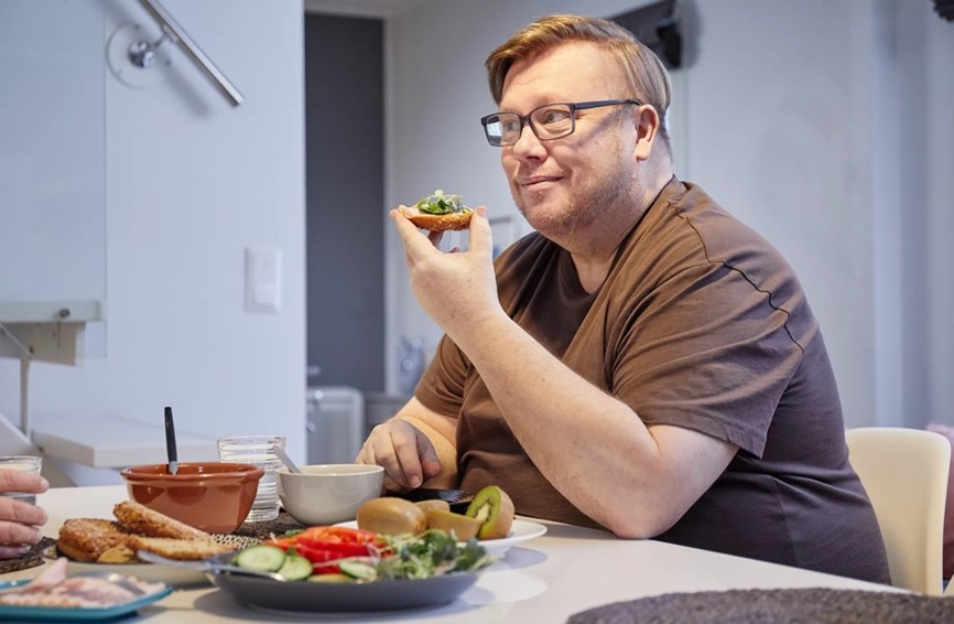 Mies syö pöydän ääressä kauraleipää, vihanneksia ja hedelmiä