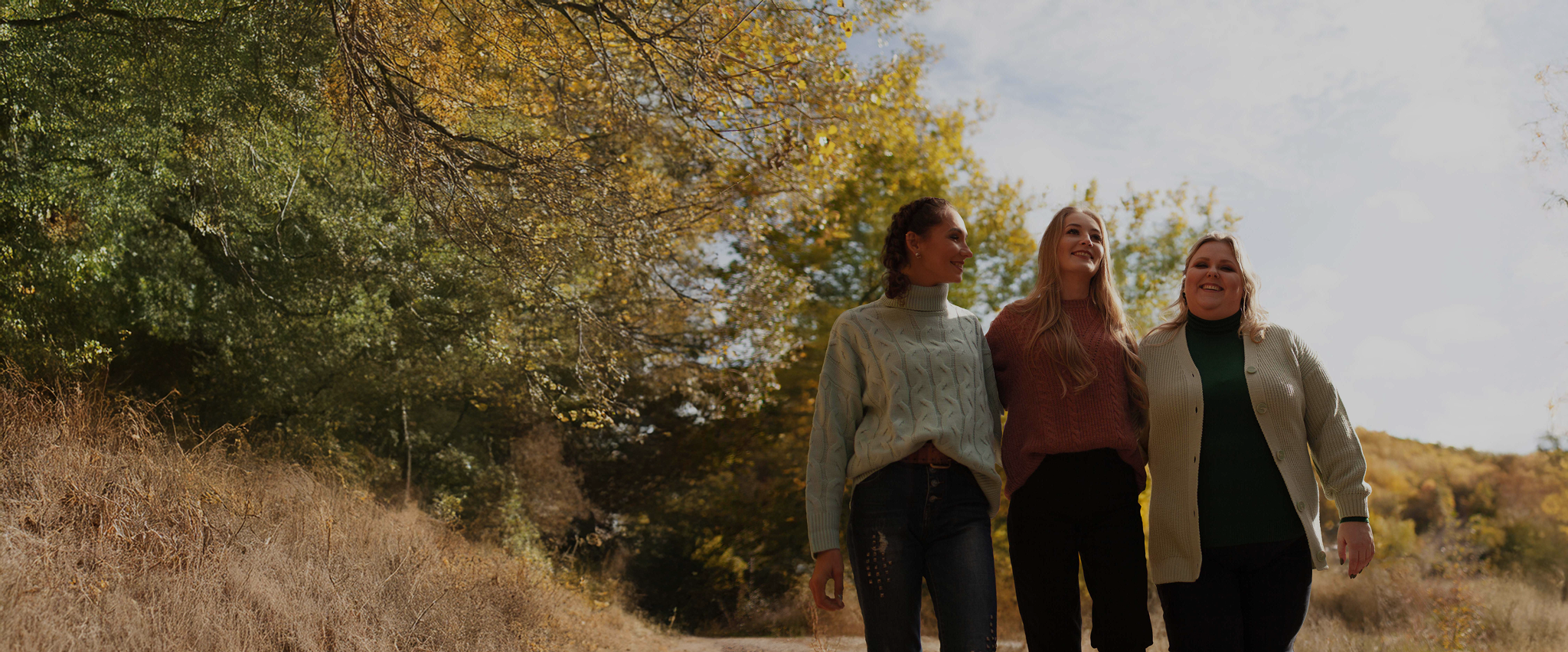 Three women walking together outdoors on a sunny day, enjoying each other’s company.