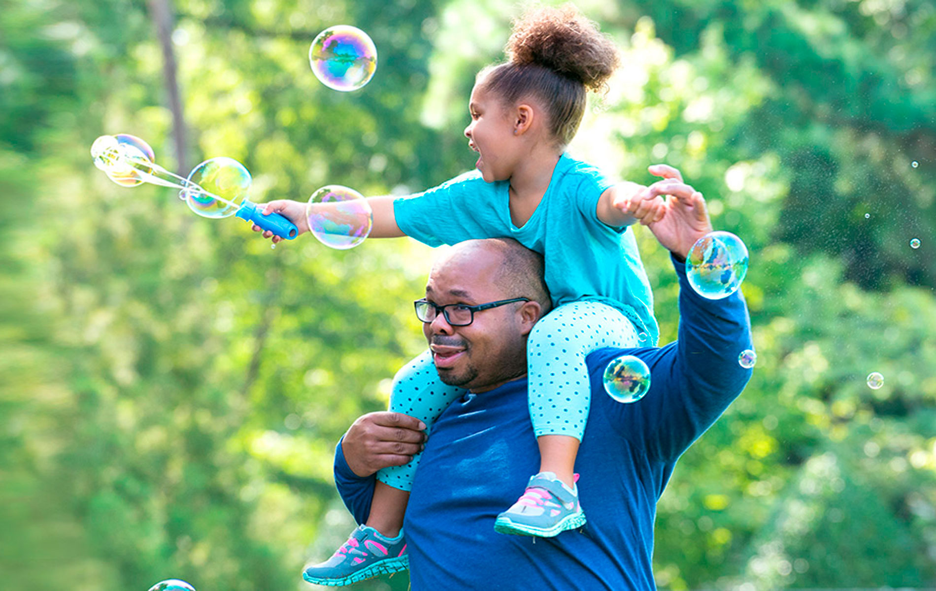 A happy father with obesity giving his daughter a piggyback ride while she joyfully blows bubbles outdoors.