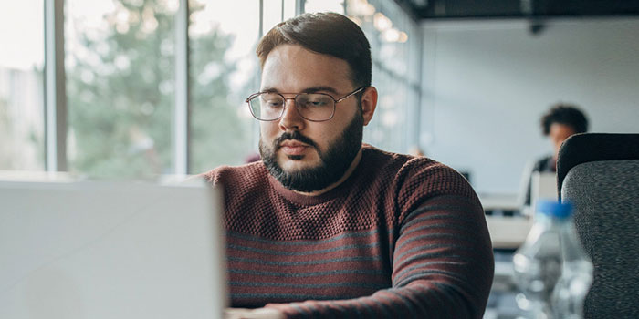 A contemplative man working on a laptop, embodying the societal pressures faced by those who do not fit the traditional masculine physique.