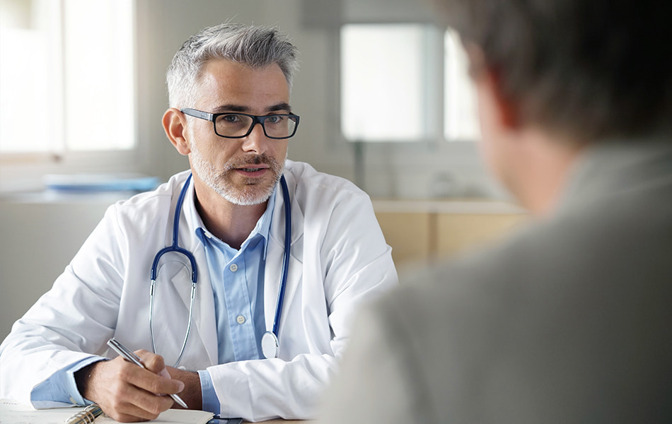 Gråhåret mannlig lege i prat med pasient