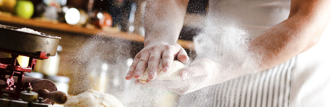 Man kneading a dough with flour flying around.