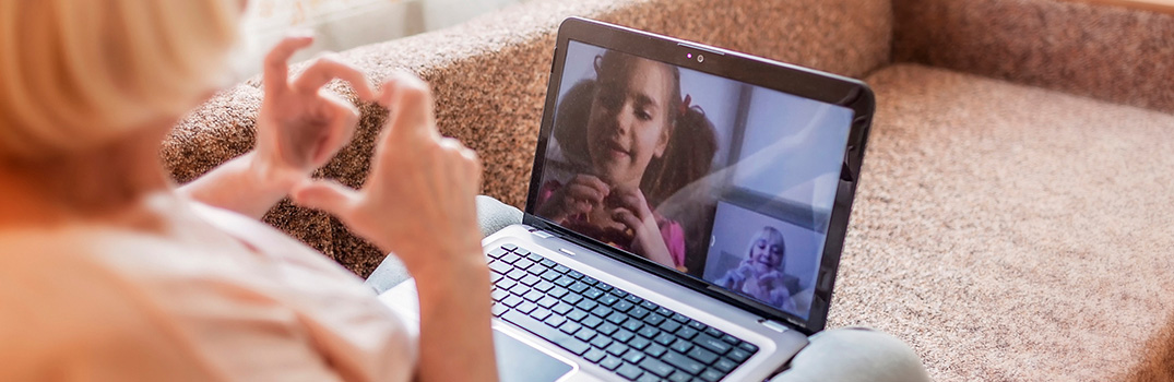 Woman making a heart gesture with her hands towards a video call with a young girl.