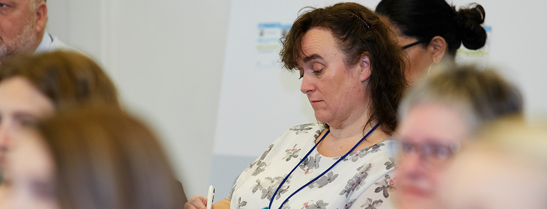 Woman at a conference looking down while writing notes.